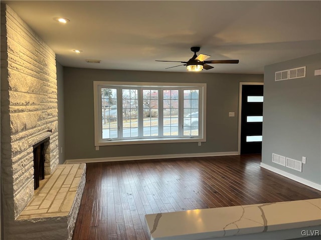 unfurnished living room with a stone fireplace, dark wood-type flooring, and ceiling fan