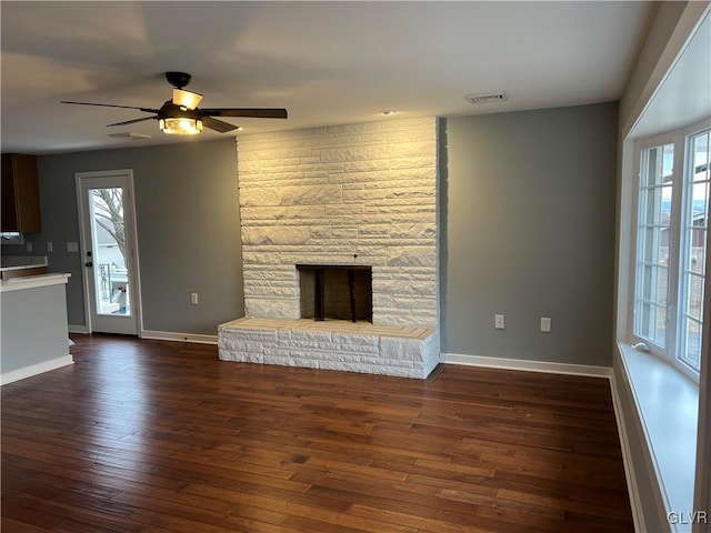 unfurnished living room with dark hardwood / wood-style flooring, a stone fireplace, and ceiling fan