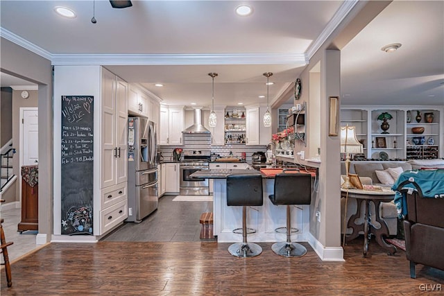 kitchen with appliances with stainless steel finishes, a kitchen breakfast bar, kitchen peninsula, white cabinets, and wall chimney range hood