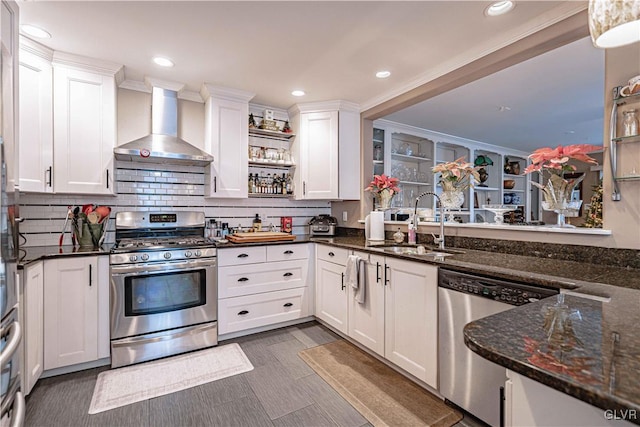 kitchen featuring wall chimney exhaust hood, sink, white cabinetry, appliances with stainless steel finishes, and dark stone counters