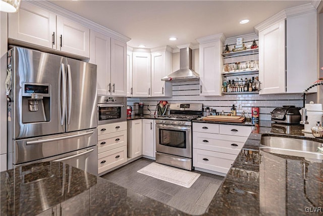 kitchen with dark stone countertops, wall chimney range hood, stainless steel appliances, and white cabinets