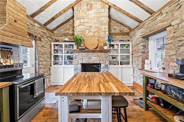 kitchen with lofted ceiling with beams, stainless steel electric stove, butcher block counters, and a fireplace