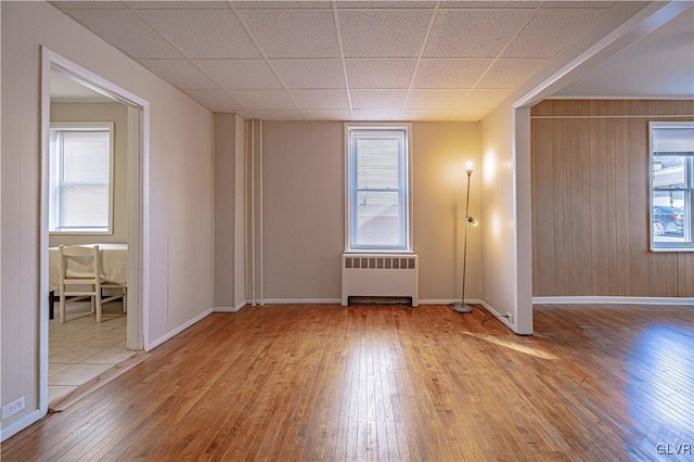 unfurnished room with a drop ceiling, radiator, wood-type flooring, and wooden walls