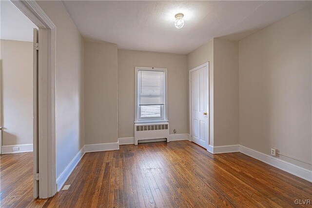 empty room featuring radiator and dark hardwood / wood-style floors