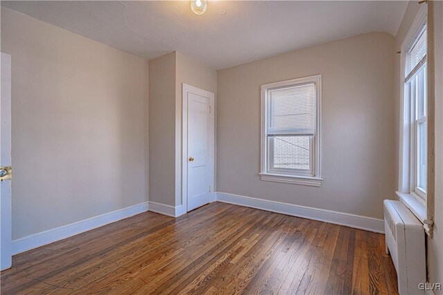 spare room with dark hardwood / wood-style flooring, radiator, and plenty of natural light