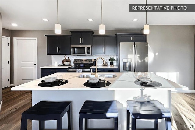 kitchen featuring pendant lighting, sink, appliances with stainless steel finishes, a kitchen breakfast bar, and an island with sink