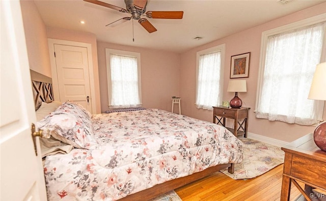 bedroom with ceiling fan, wood-type flooring, and multiple windows