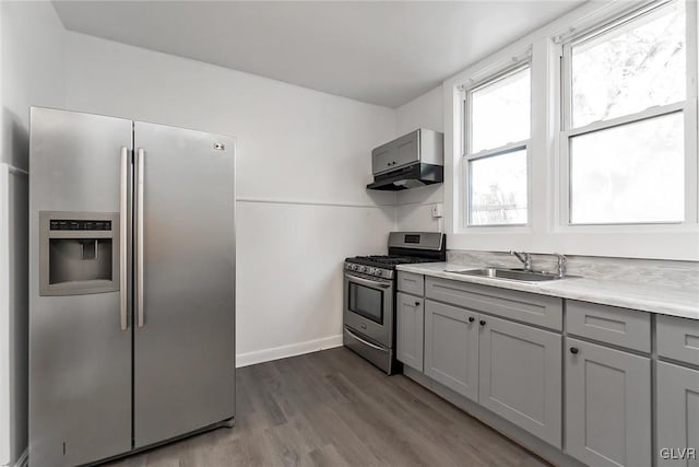 kitchen with sink, wall chimney range hood, gray cabinets, stainless steel appliances, and light hardwood / wood-style floors