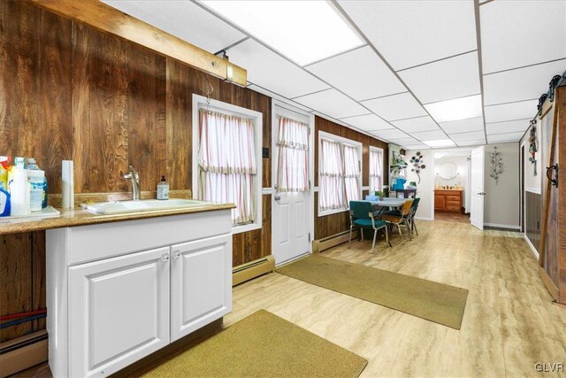 kitchen with sink, light hardwood / wood-style flooring, baseboard heating, wooden walls, and white cabinets