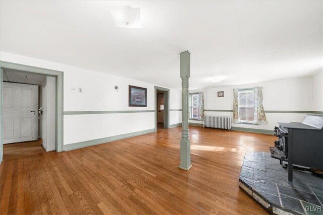 unfurnished living room featuring radiator heating unit, wood-type flooring, and a wood stove