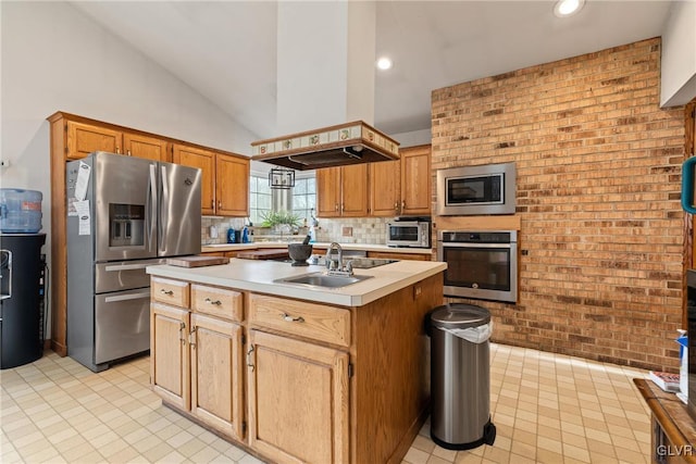 kitchen with brick wall, appliances with stainless steel finishes, an island with sink, sink, and island exhaust hood