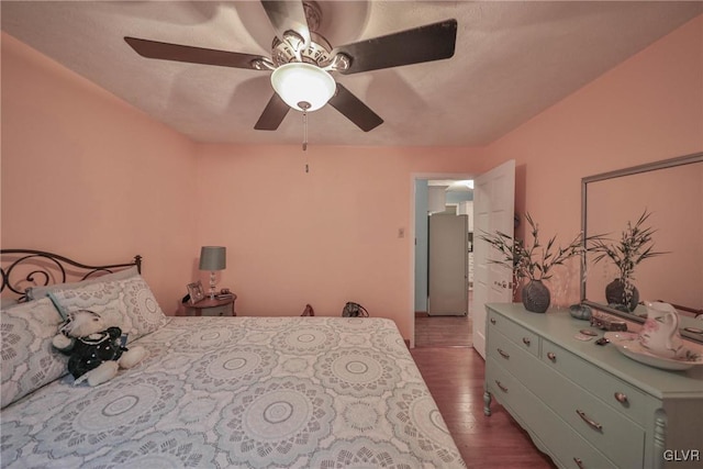 bedroom with dark hardwood / wood-style flooring, stainless steel fridge, and ceiling fan