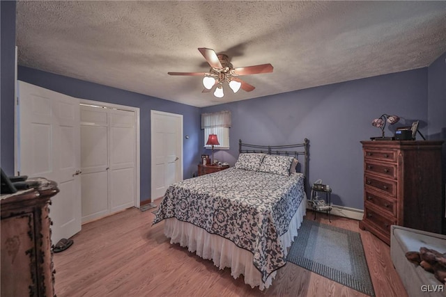 bedroom with multiple closets, ceiling fan, light hardwood / wood-style flooring, and a textured ceiling