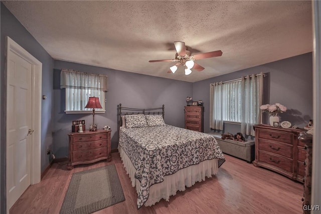 bedroom with multiple windows, ceiling fan, wood-type flooring, and a textured ceiling