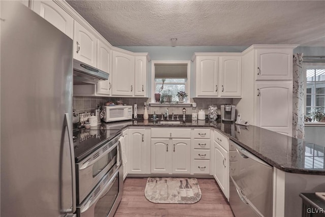 kitchen featuring white cabinetry, dark stone counters, kitchen peninsula, stainless steel appliances, and dark wood-type flooring