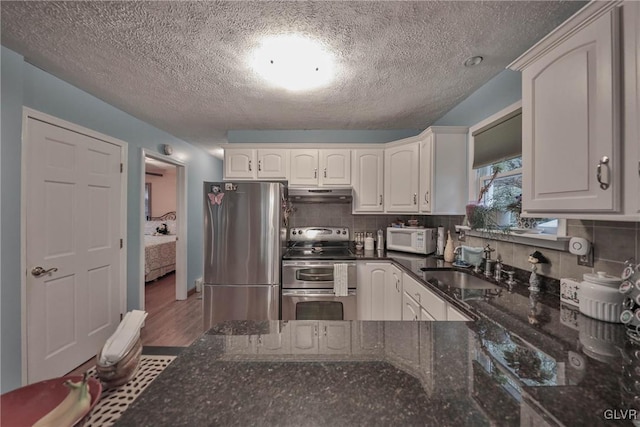 kitchen featuring appliances with stainless steel finishes, tasteful backsplash, sink, dark stone countertops, and white cabinets