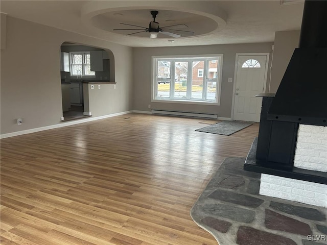 unfurnished living room featuring a baseboard radiator, sink, ceiling fan, and light wood-type flooring