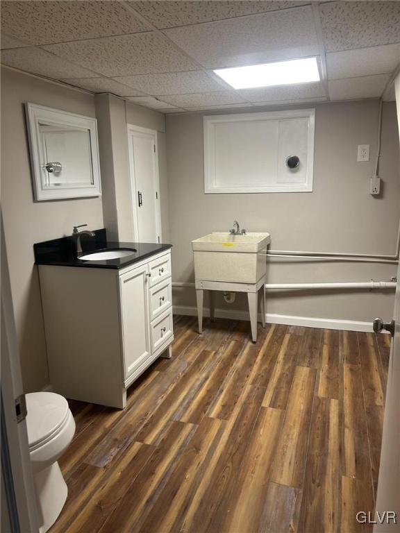 bathroom featuring vanity, wood-type flooring, toilet, and a drop ceiling