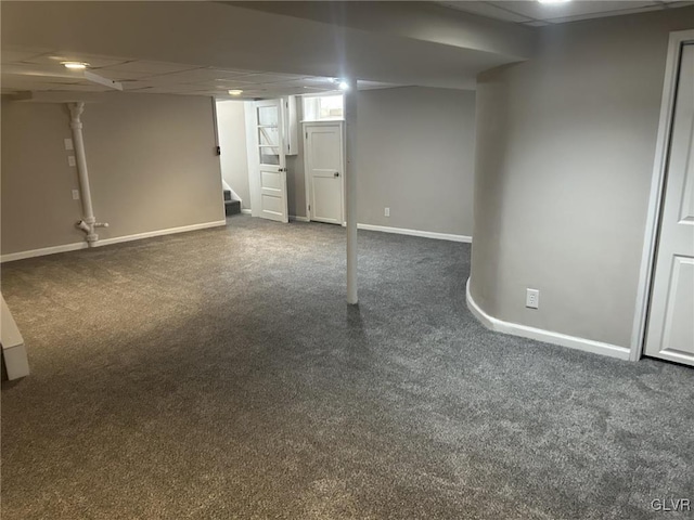 basement with a paneled ceiling and dark carpet