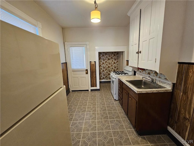 kitchen featuring sink, decorative light fixtures, dark brown cabinets, fridge, and white gas range