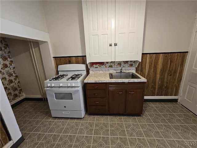 kitchen with wooden walls, white gas range, sink, and dark brown cabinets