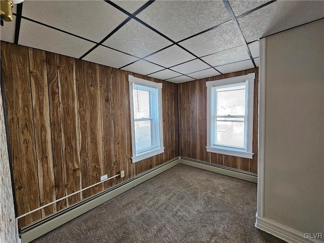 carpeted empty room with a drop ceiling, a healthy amount of sunlight, and wood walls