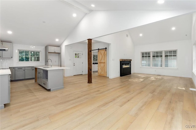 kitchen with sink, a center island with sink, light wood-type flooring, gray cabinets, and a barn door