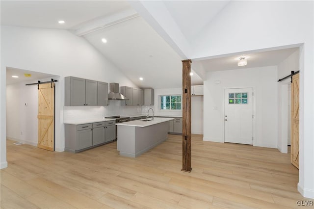 kitchen with gray cabinetry, wall chimney range hood, a barn door, and a center island with sink