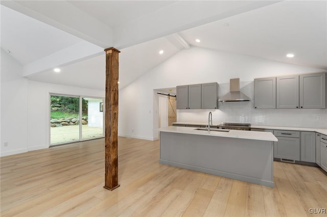 kitchen with sink, gray cabinetry, an island with sink, light hardwood / wood-style floors, and wall chimney range hood