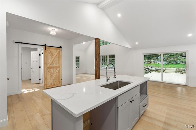 kitchen with sink, light stone counters, gray cabinets, a barn door, and a kitchen island with sink