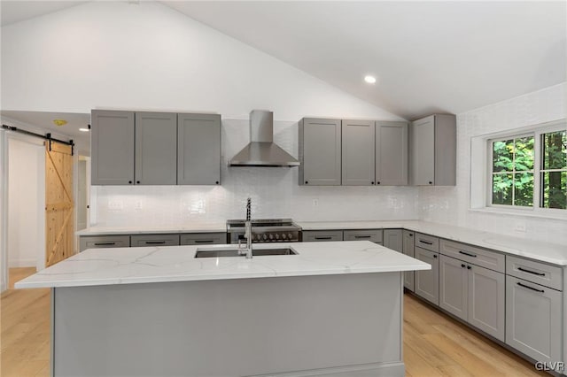 kitchen featuring sink, gray cabinets, a kitchen island with sink, light stone countertops, and wall chimney exhaust hood