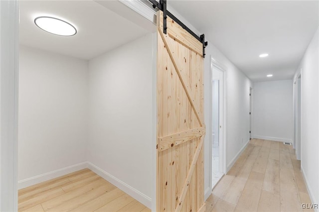 corridor with a barn door and light hardwood / wood-style flooring