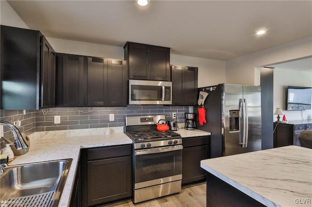 kitchen with sink, appliances with stainless steel finishes, backsplash, dark brown cabinets, and light hardwood / wood-style floors