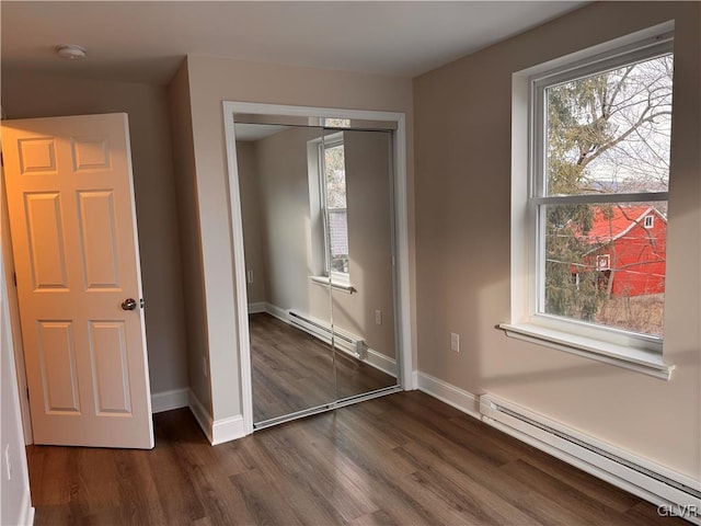 unfurnished bedroom with dark wood-type flooring, multiple windows, a closet, and a baseboard heating unit