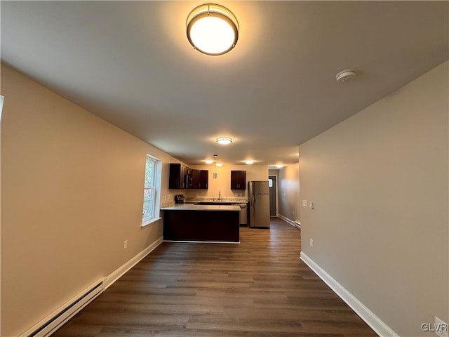 kitchen featuring dark wood-type flooring, dark brown cabinets, baseboard heating, stainless steel refrigerator, and kitchen peninsula