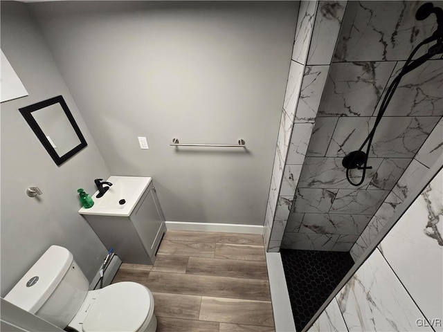 bathroom featuring a tile shower, vanity, toilet, and a baseboard heating unit