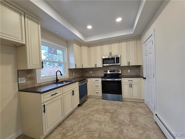 kitchen with sink, a baseboard heating unit, stainless steel appliances, a raised ceiling, and cream cabinetry