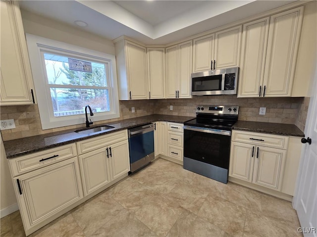 kitchen featuring appliances with stainless steel finishes, tasteful backsplash, sink, dark stone countertops, and cream cabinets