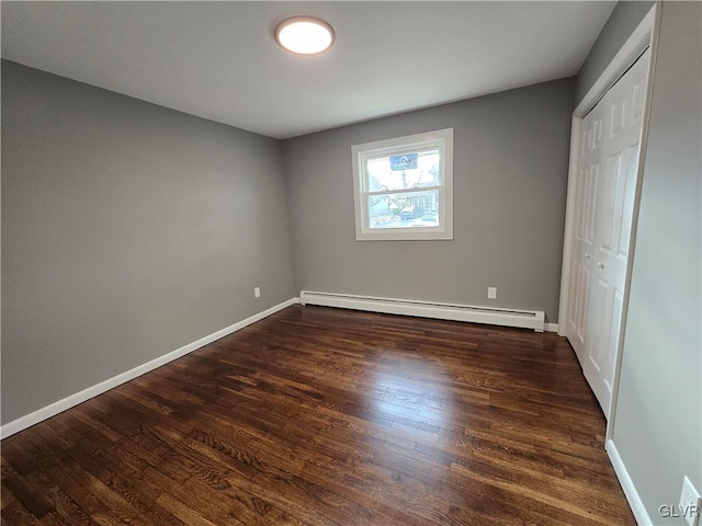 unfurnished bedroom featuring a baseboard heating unit, dark hardwood / wood-style floors, and a closet