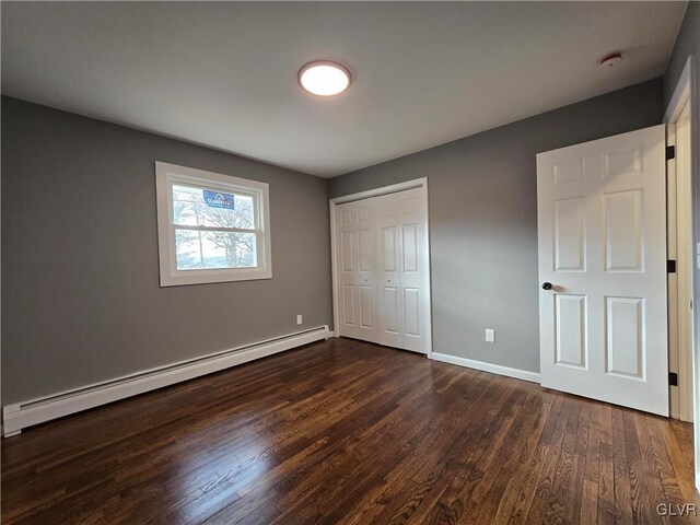 unfurnished bedroom featuring dark hardwood / wood-style flooring, baseboard heating, and a closet