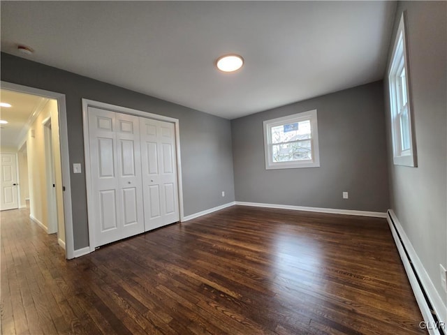 unfurnished bedroom featuring dark hardwood / wood-style flooring, a closet, and baseboard heating