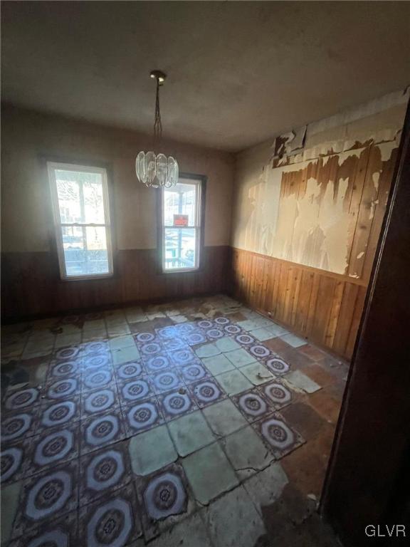 unfurnished dining area with wooden walls and a chandelier