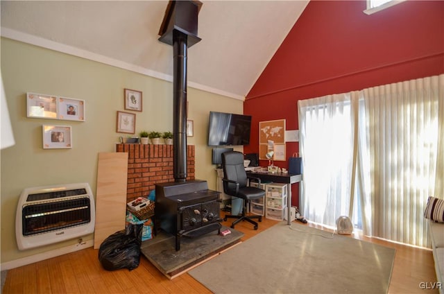 living room with lofted ceiling, hardwood / wood-style flooring, heating unit, ornamental molding, and a wood stove