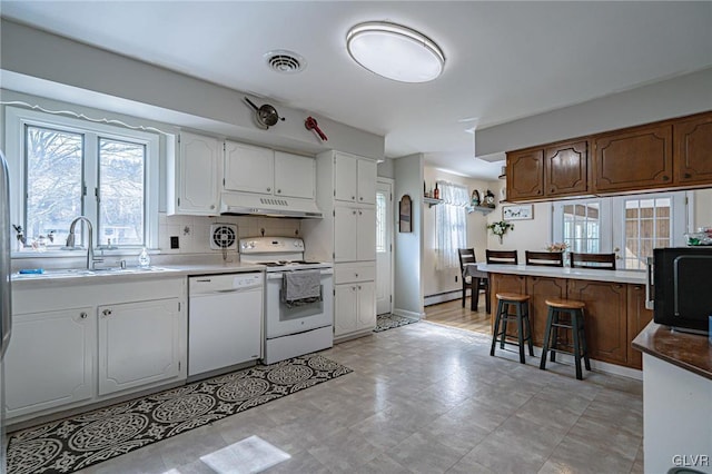 kitchen featuring sink, white appliances, a breakfast bar area, backsplash, and white cabinets