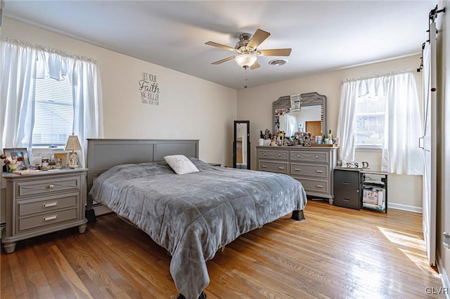 bedroom featuring light hardwood / wood-style flooring, a barn door, and ceiling fan