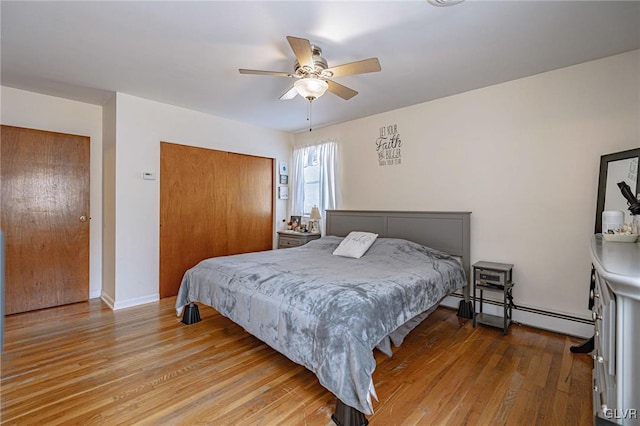 bedroom with wood-type flooring, ceiling fan, a baseboard radiator, and a closet