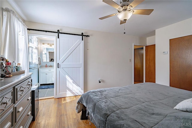 bedroom featuring ceiling fan, connected bathroom, a barn door, and light hardwood / wood-style flooring