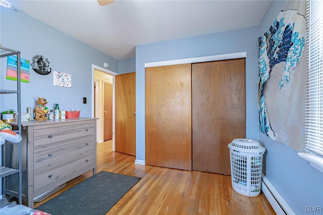 bedroom with a closet, baseboard heating, and light hardwood / wood-style flooring