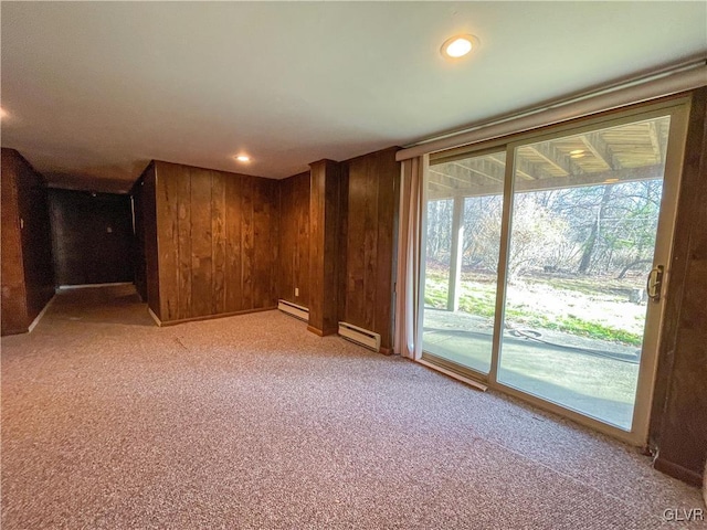 carpeted spare room featuring a baseboard heating unit and wood walls