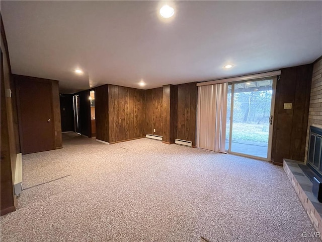 unfurnished living room featuring a baseboard radiator, wooden walls, light colored carpet, and a brick fireplace